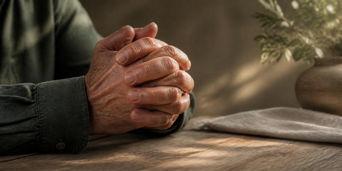 The Praying Hands: A Story of Great Sacrifice Older hands folded in prayer over an open Bible in warm window light
